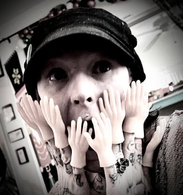 Kristen Tomaru in a cap, mouth open in mock horror, surrounded by tiny rubber hands